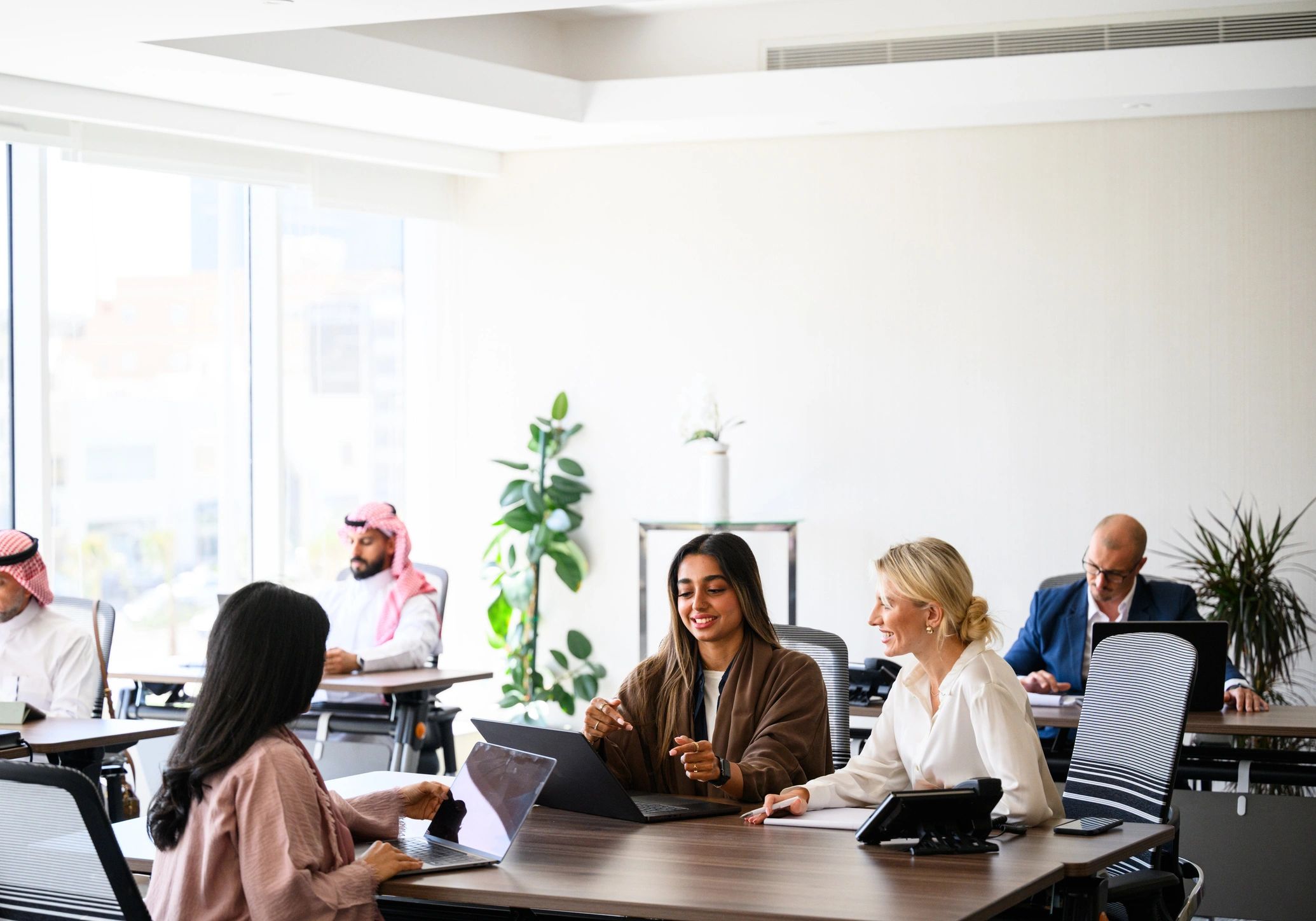 Wide view of diverse business women having a discussion while sitting with laptops in a bright modern workspace